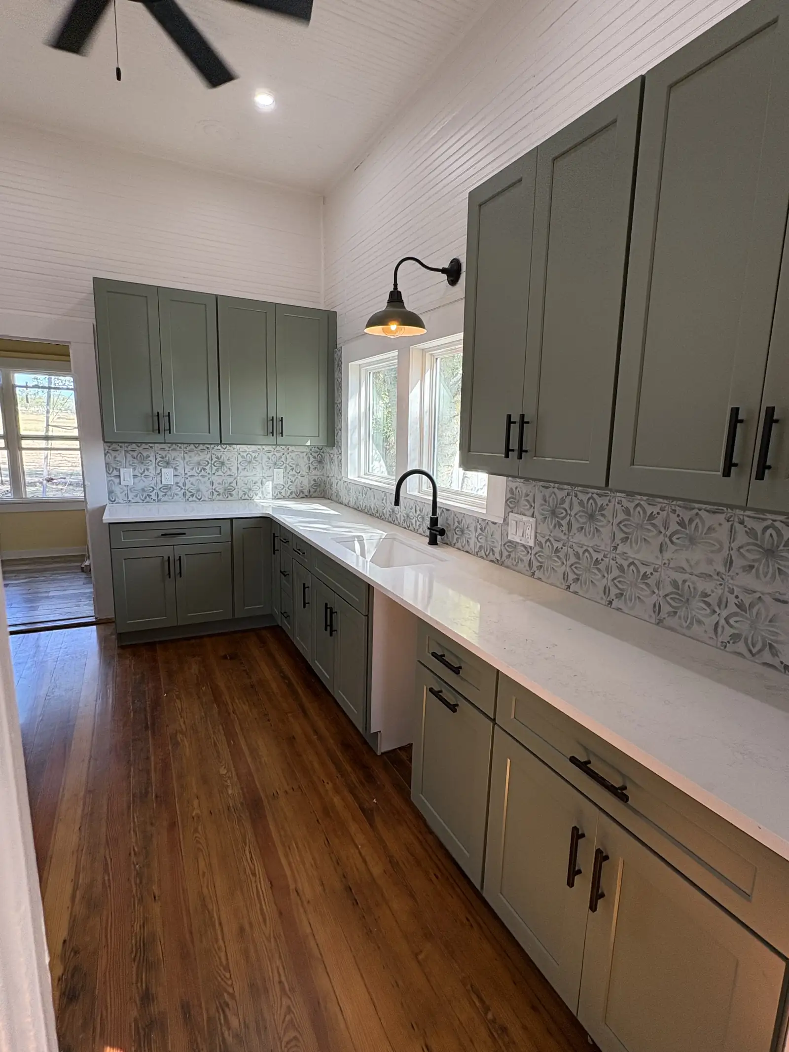 Restored Hill Country farmhouse kitchen with sage green cabinets and open wood shelving