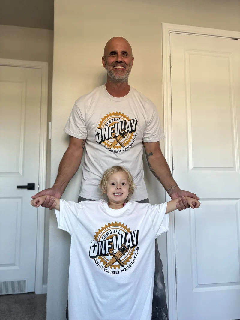 Hayne Wolmarans at home holding up a OneWay Remodel shirt beside a young member of his family wearing a matching one