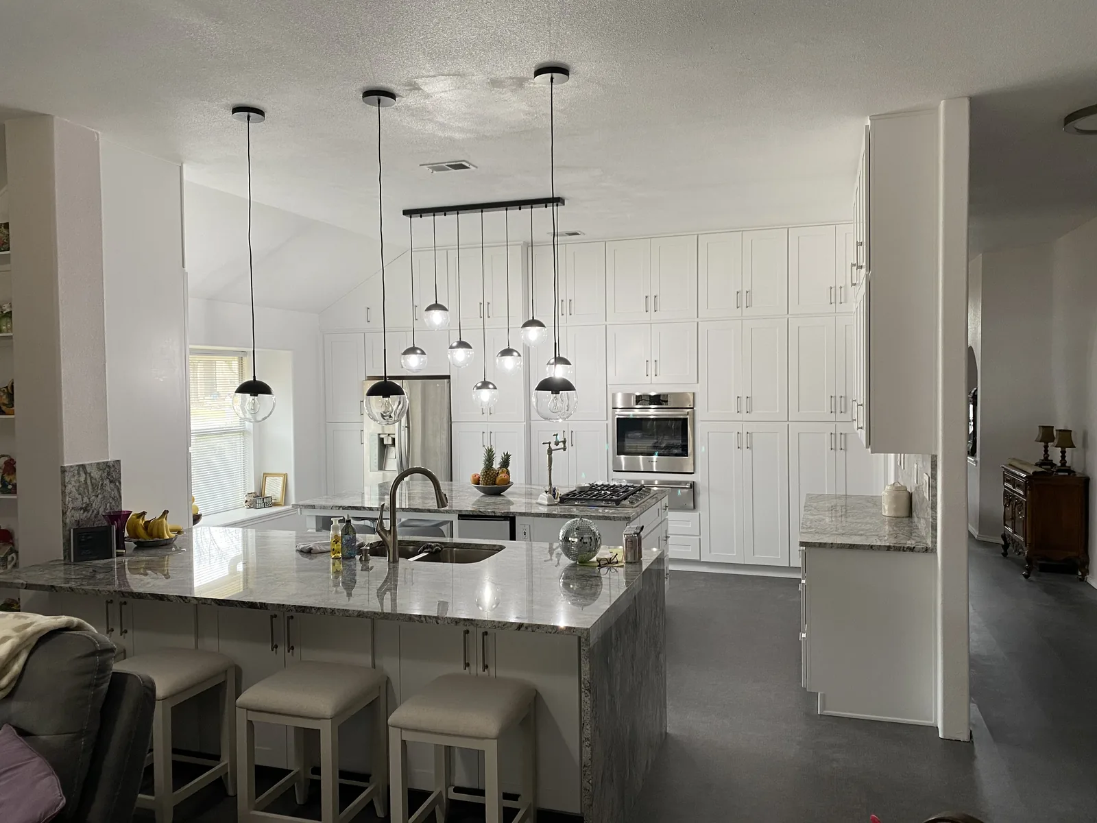 White kitchen with a waterfall stone island and a cluster of pendant lights