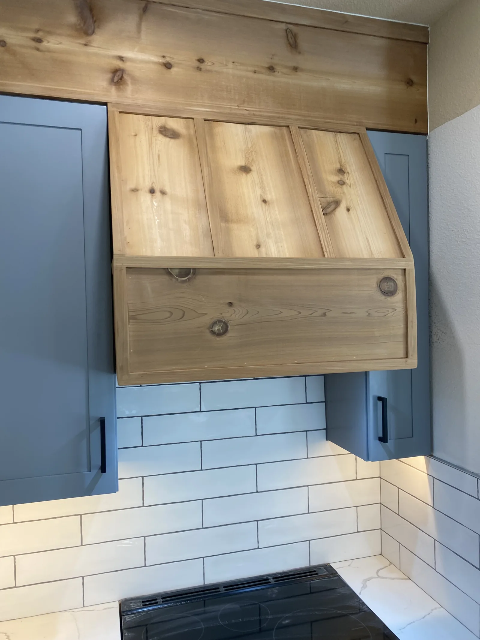 Detail of a knotty cedar range hood against white subway tile